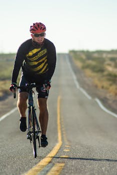 A cyclist wearing a helmet is riding a bike on a long, open road during the day.