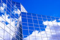 现代玻璃建筑在低角度视角下，将云层映照在鲜艳的蓝天上