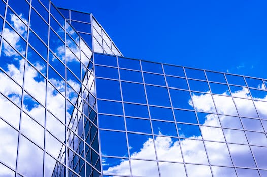 现代玻璃建筑在低角度视角下，将云层映照在鲜艳的蓝天上