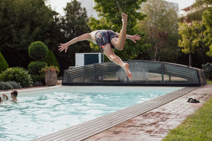 A boy jumping into a backyard swimming pool on a sunny day