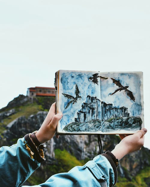 Woman Hands Holding Painting of Dragons Flying over Castle