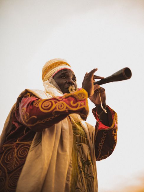 African man in vibrant traditional clothing playing musical instrument outdoors in Nigeria.