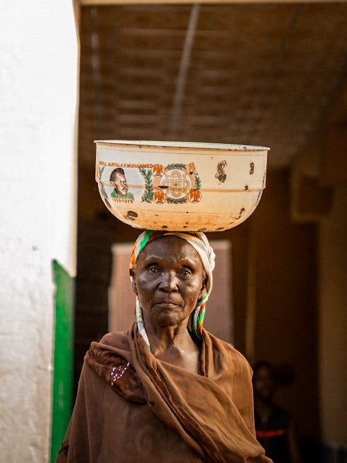 Photo of an Elderly Woman with a Bowl on Her Head 
