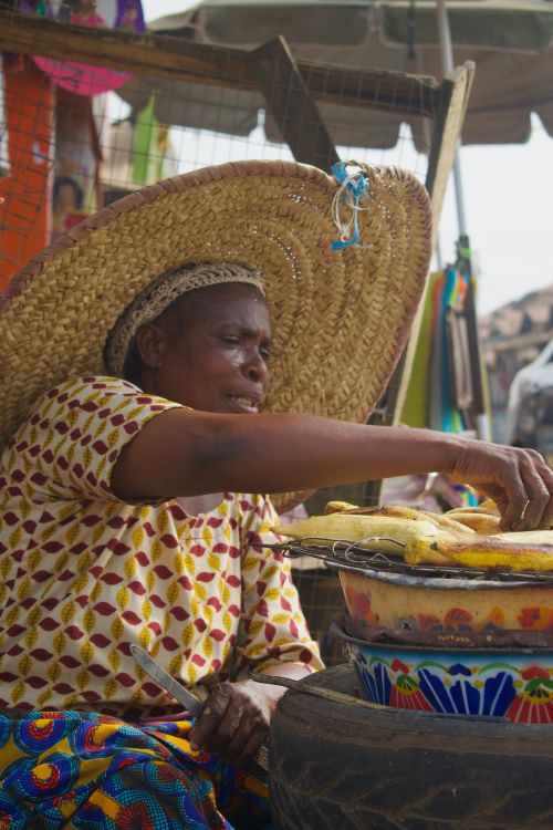 Free A woman in a large straw hat prepares street food at an outdoor market setting. Stock Photo