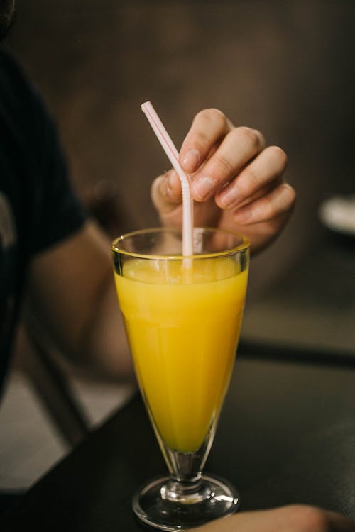 Man Hand Holding Straw in Juice Glass