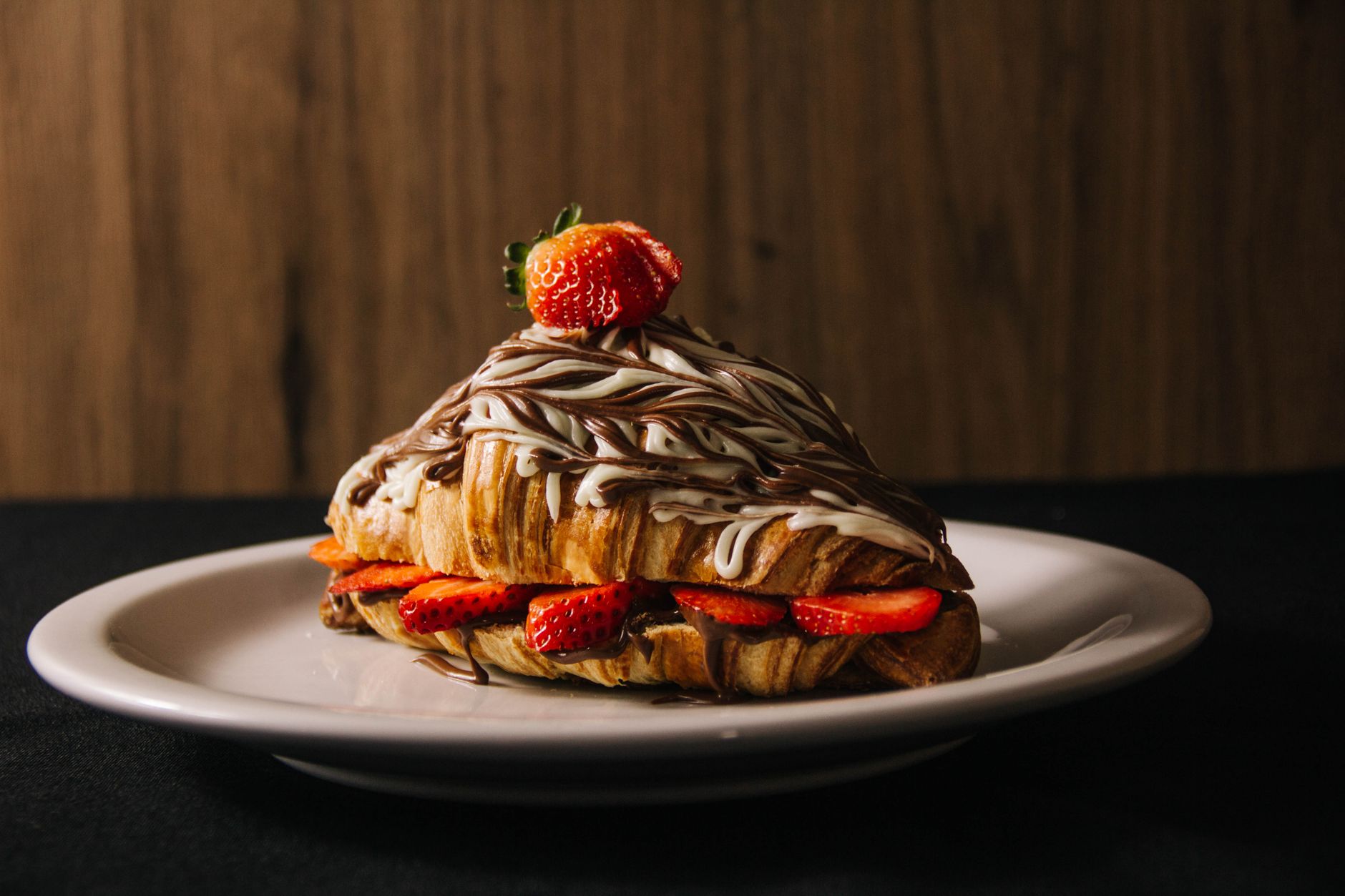 A tempting croissant filled with strawberries and drizzled with chocolate on a plate.
