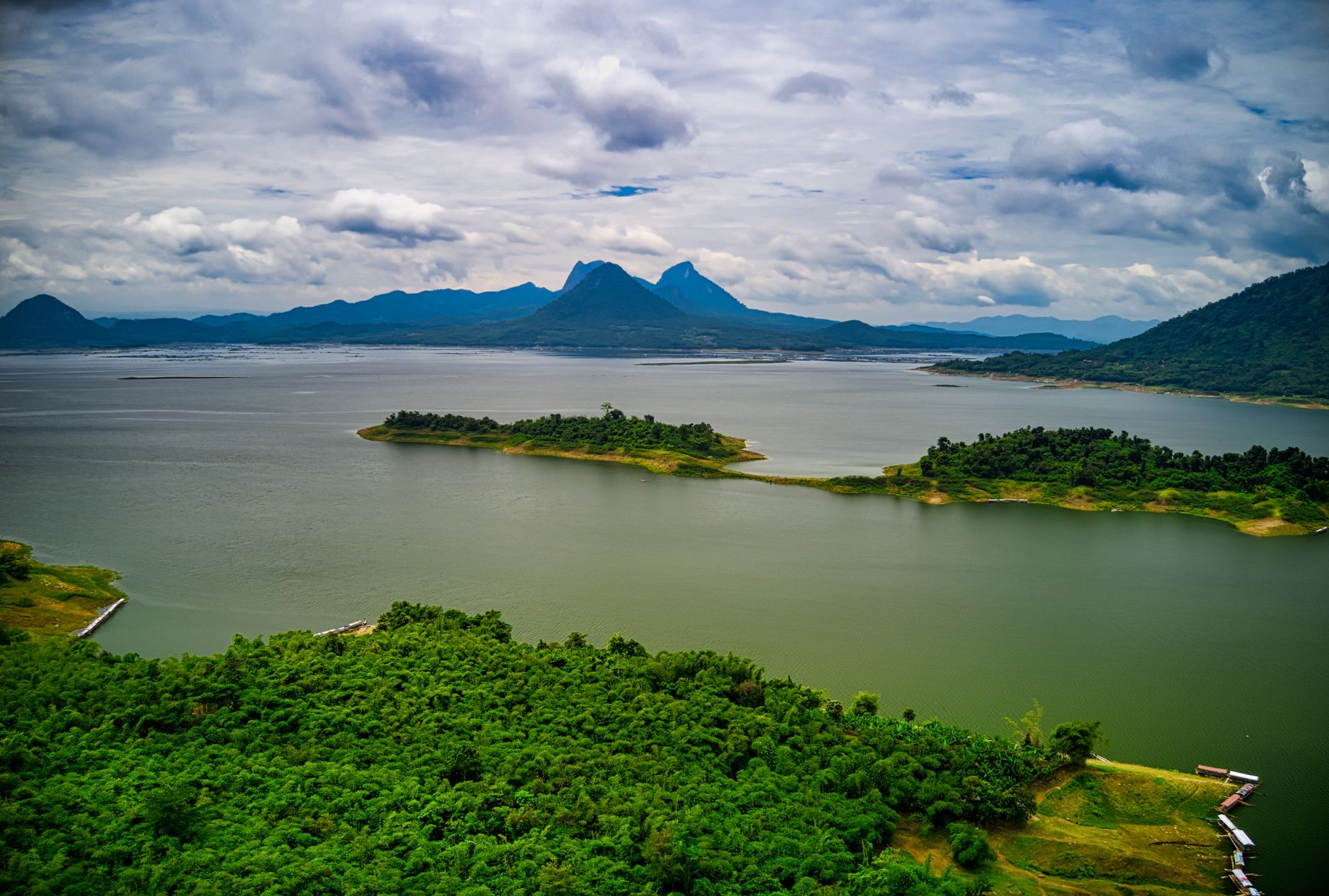 Stunning aerial view of lush green islands against a backdrop of mountains and serene lake in Purwakarta, Indonesia.