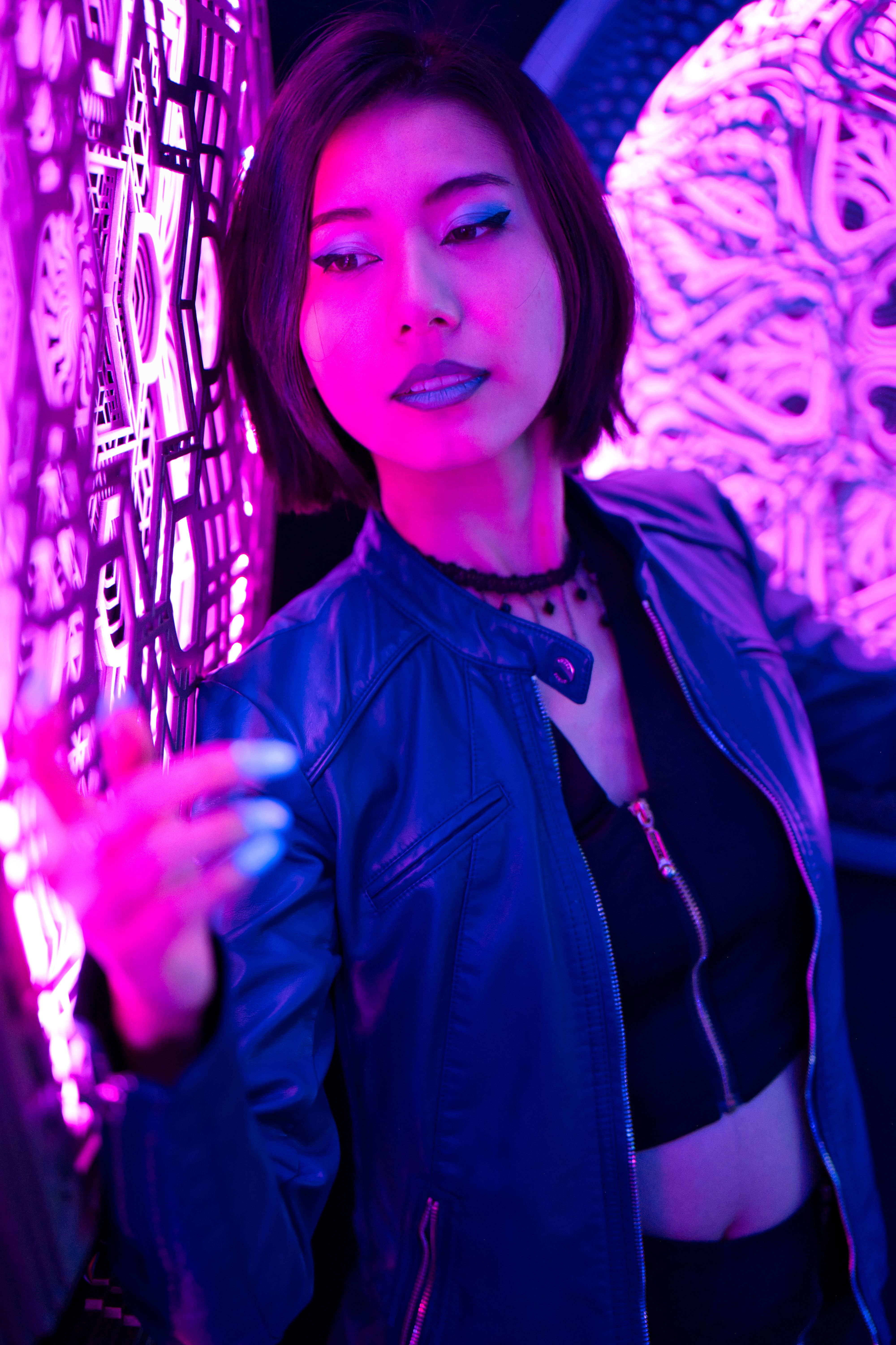 Fashionable woman posing in purple lighting wearing a leather jacket and crop top.