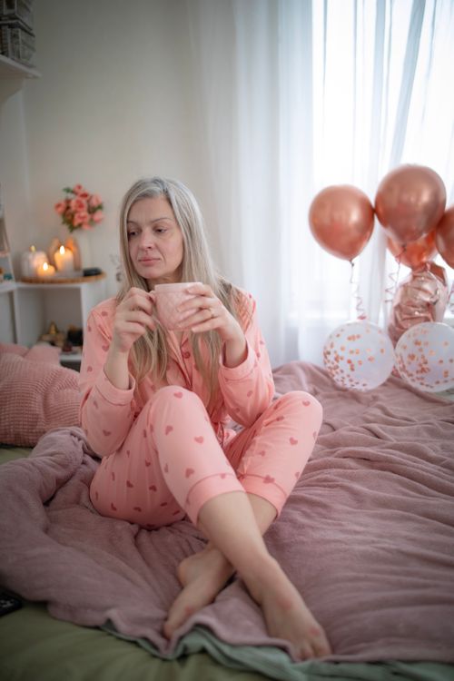 Free A woman in pink pajamas enjoys a morning coffee surrounded by balloons in a cozy bedroom. Stock Photo