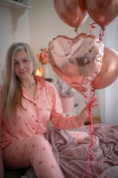 Woman in heart-patterned pajamas holding balloons indoors, creating a cozy Valentine's vibe.