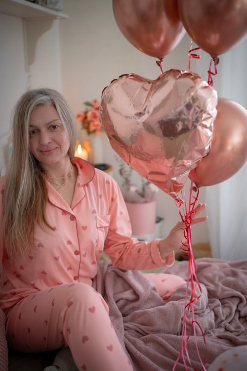 Free Woman in heart-patterned pajamas holding balloons indoors, creating a cozy Valentine's vibe. Stock Photo