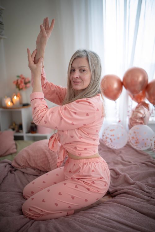 Free Blonde woman in pink heart-patterned pajamas posing with balloons in a cozy indoor setting. Stock Photo