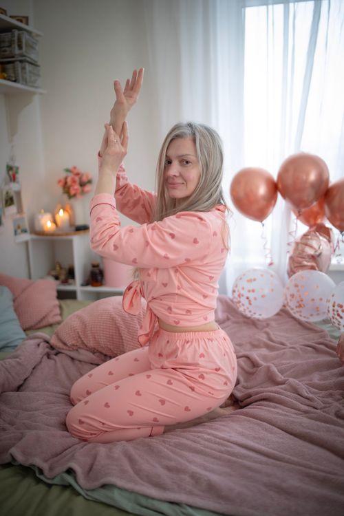 Free Blonde woman in pink heart pajamas posing on bed with decorative balloons. Stock Photo