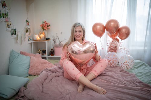 Free Blonde Woman Sitting with Balloons on Bed Stock Photo