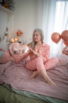 Cozy indoor scene of a woman in pink pajamas holding a heart-shaped balloon.