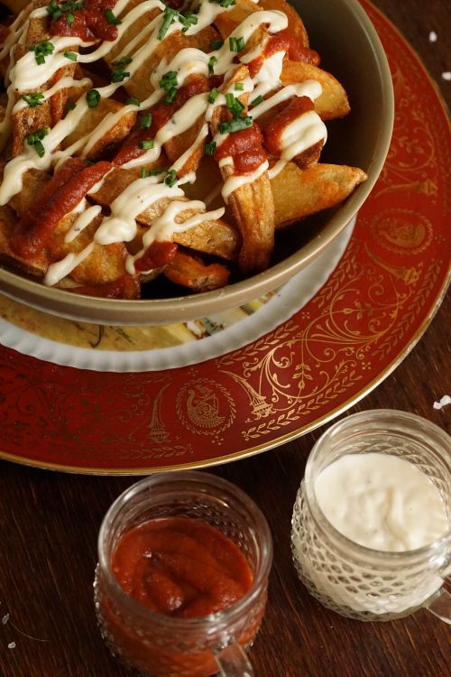 Free Crispy potato wedges drizzled with mayonnaise and ketchup, served on an ornate plate. Stock Photo