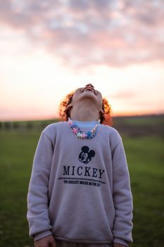 A child wearing a sweater laughs joyfully outdoors at sunset.