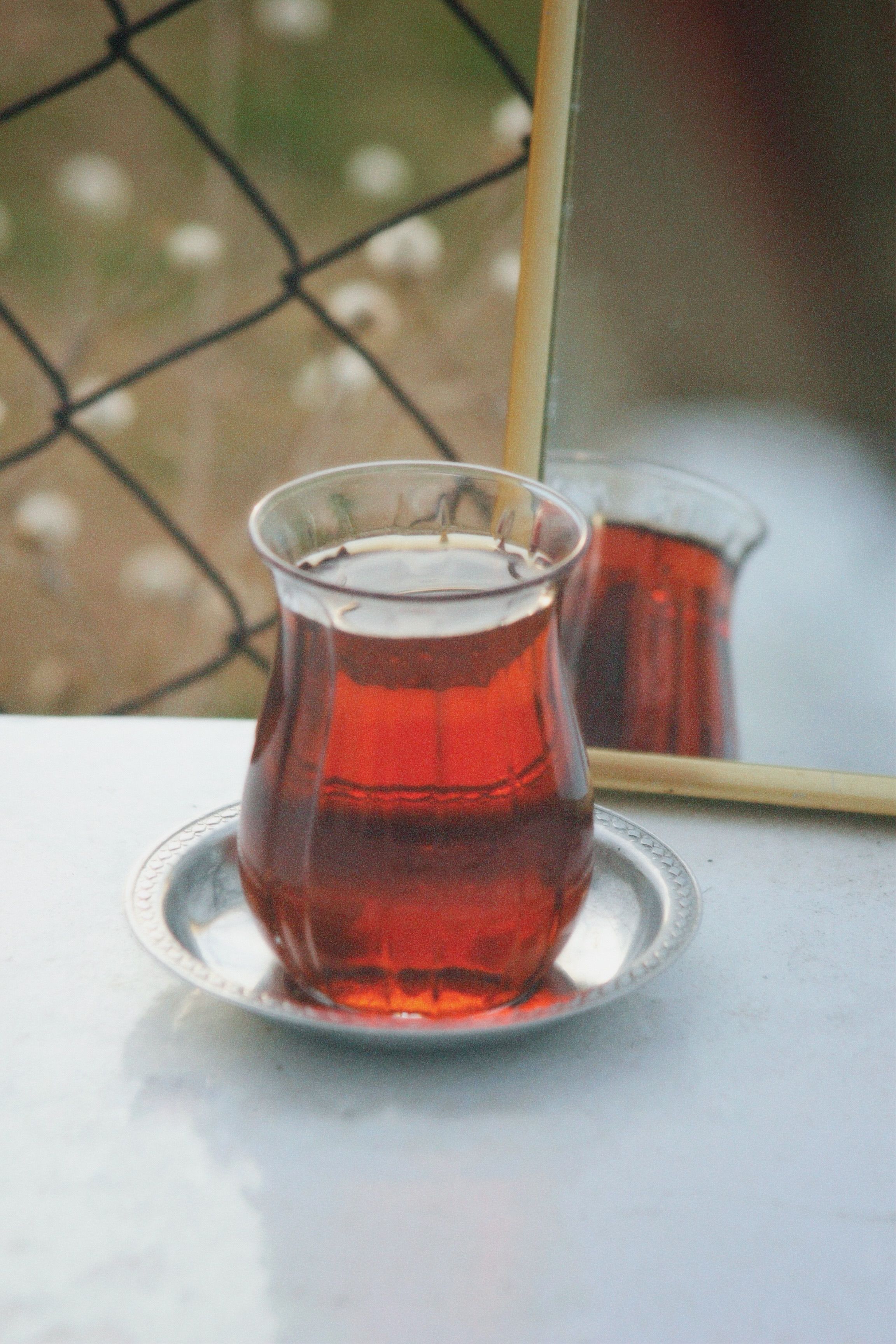 Glass of Turkish tea on a saucer outdoors, reflected in a mirror.