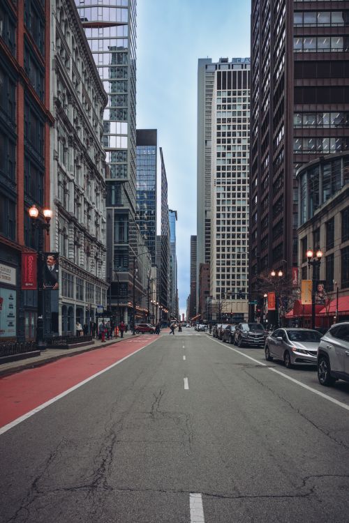 Free A bustling urban street flanked by tall skyscrapers and modern building facades under a clear sky. Stock Photo
