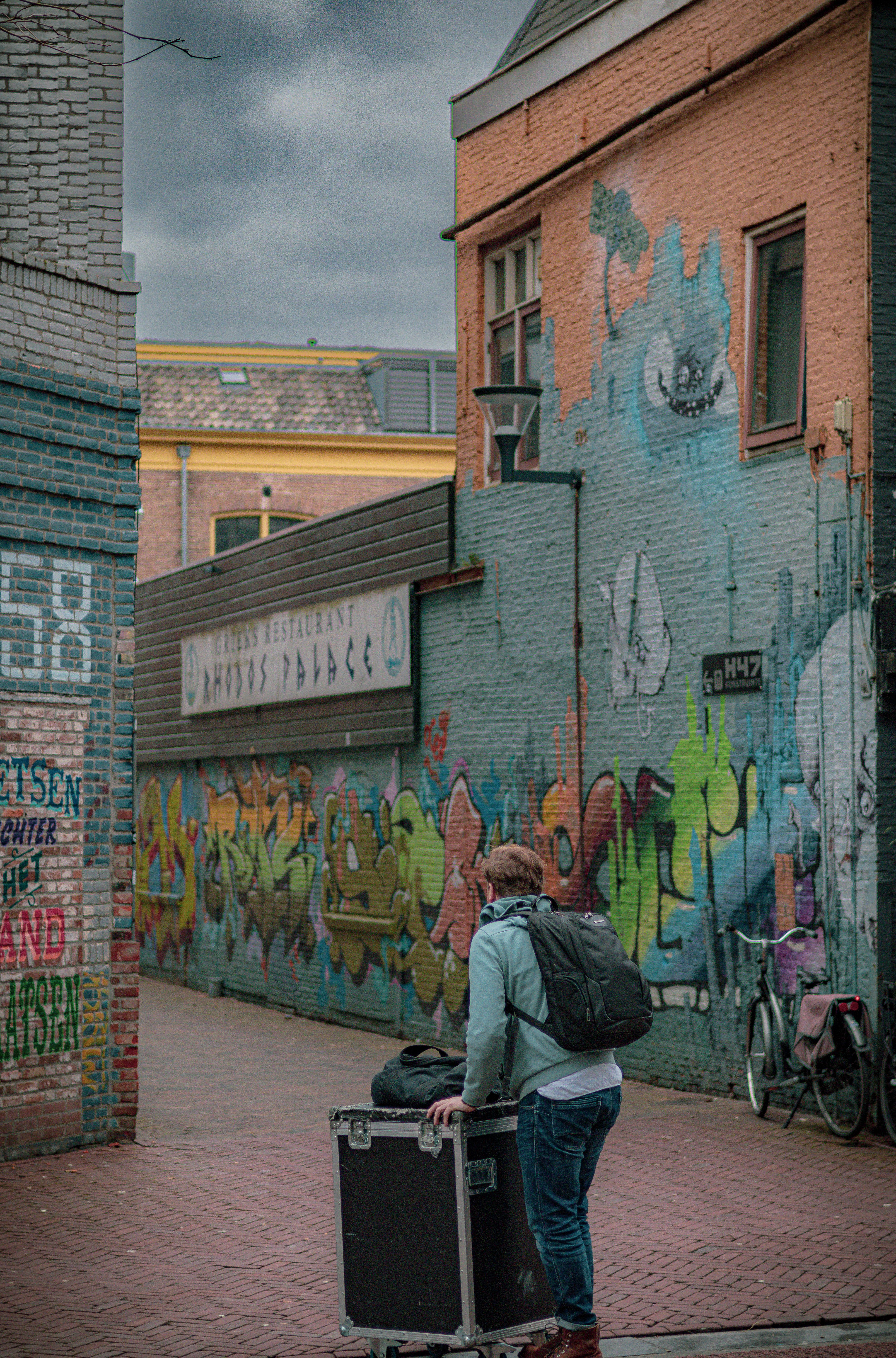 A man with a backpack strolling through a graffiti-covered alley in Leeuwarden, Netherlands.
