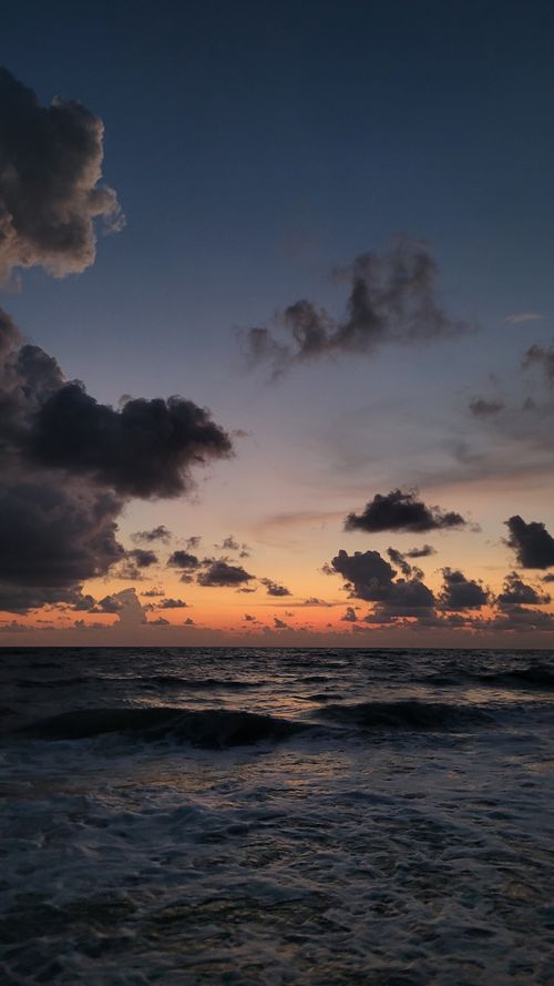 Free A breathtaking sunset view over a calm ocean with dramatic clouds and gentle waves. Stock Photo