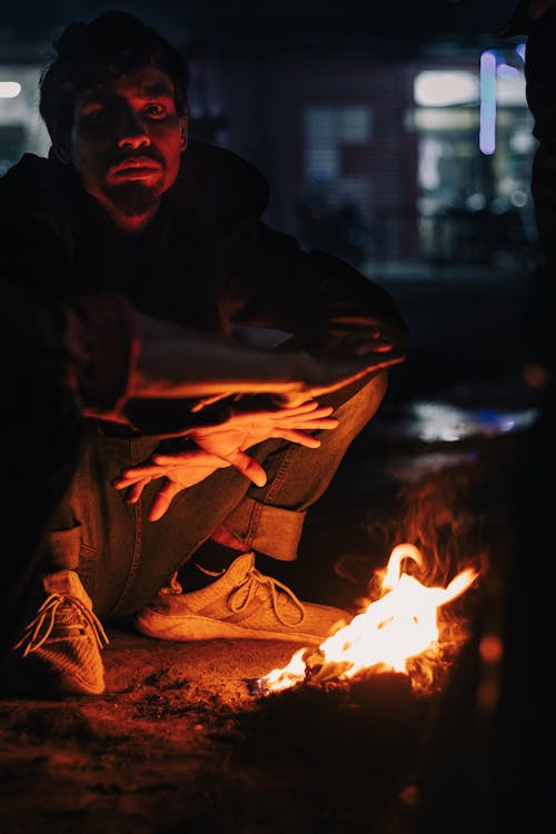 Man Squatting by Bonfire at Night