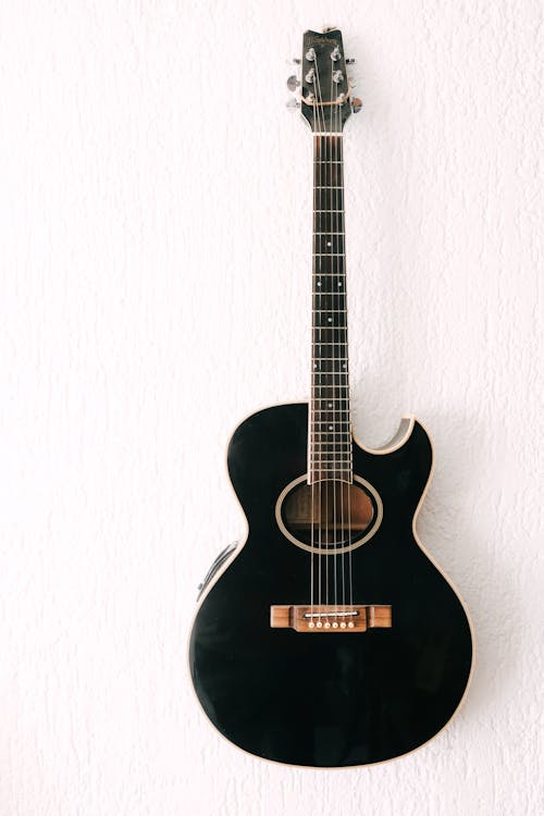 A black acoustic guitar against a white wall
