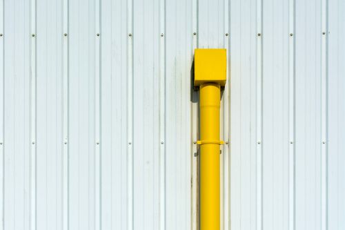 Free A vibrant yellow pipe stands out against a white corrugated metal wall, creating a striking contrast. Stock Photo