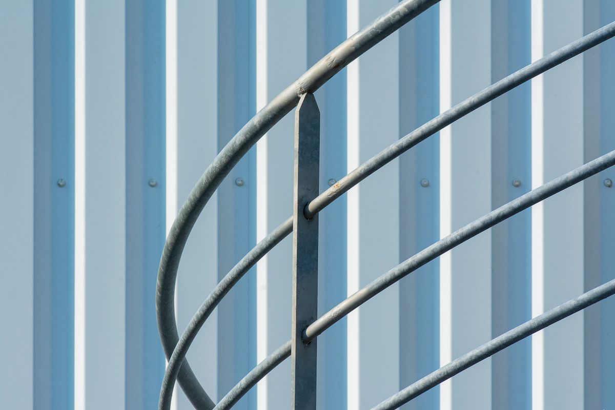 Balustradă metalică văzută de aproape, pe fundal cu perete din tablă ondulată
