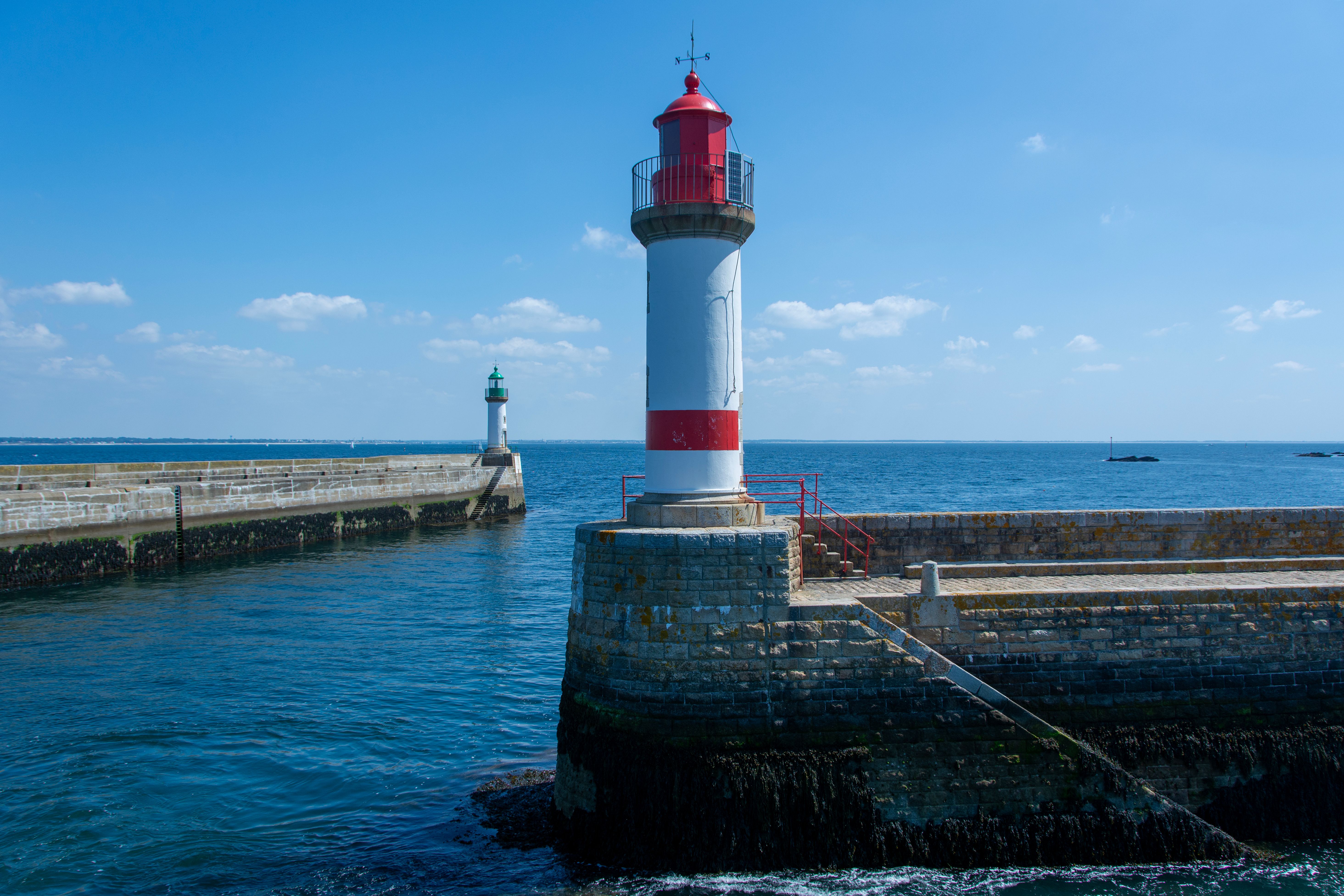 Two vibrant lighthouses on a stone pier overlooking a calm ocean under clear blue skies.