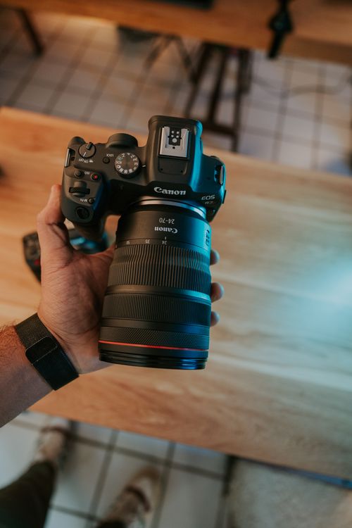 Free A person's hand holding a camera above a wooden table indoors, showcasing photography gear. Stock Photo