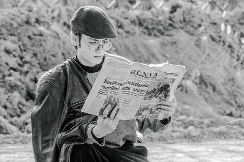 Free Stylish man in ivy cap and glasses reading a newspaper outdoors in a rural setting. Stock Photo