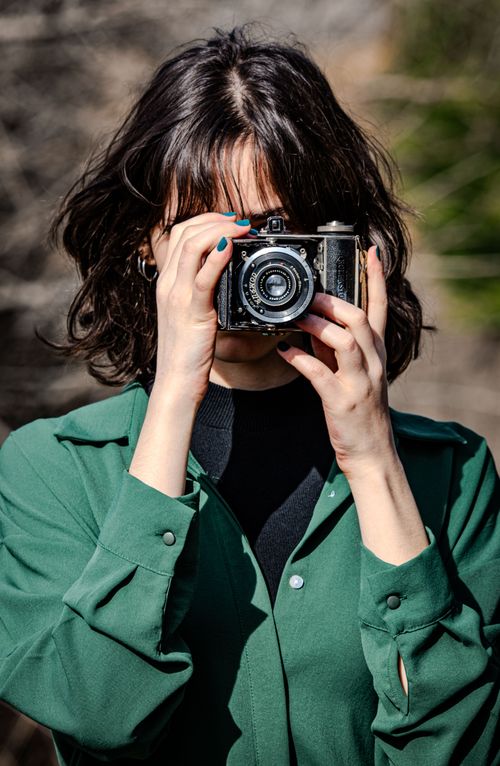 Free Woman in green shirt using vintage camera outdoors, capturing the moment. Stock Photo