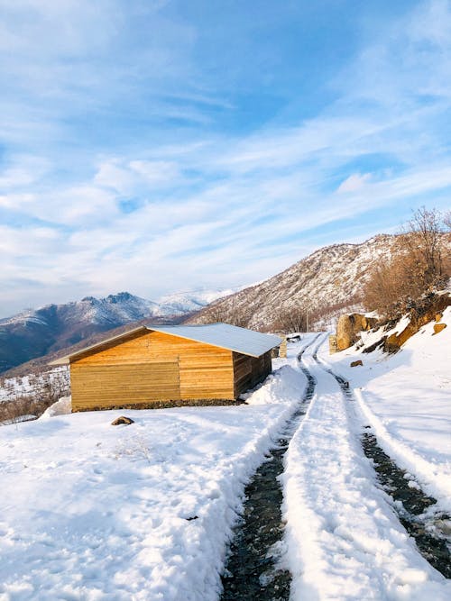 Snow around Wooden House by Dirt Road in Mountains