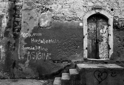 Black and white photo of an old building with graffiti and a weathered door.