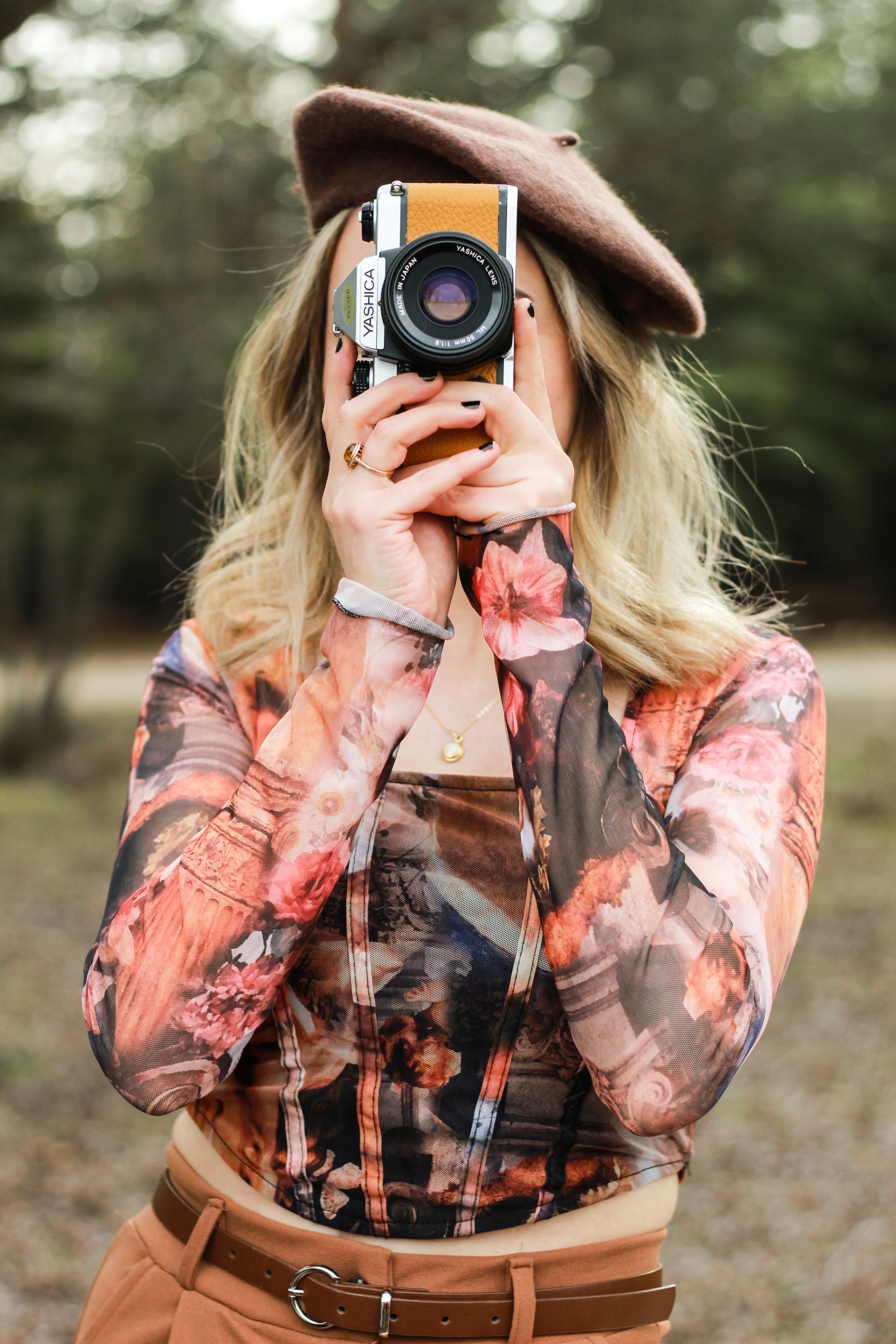 Blonde woman in a beret photographing in a park. Artistic and modern vibe.