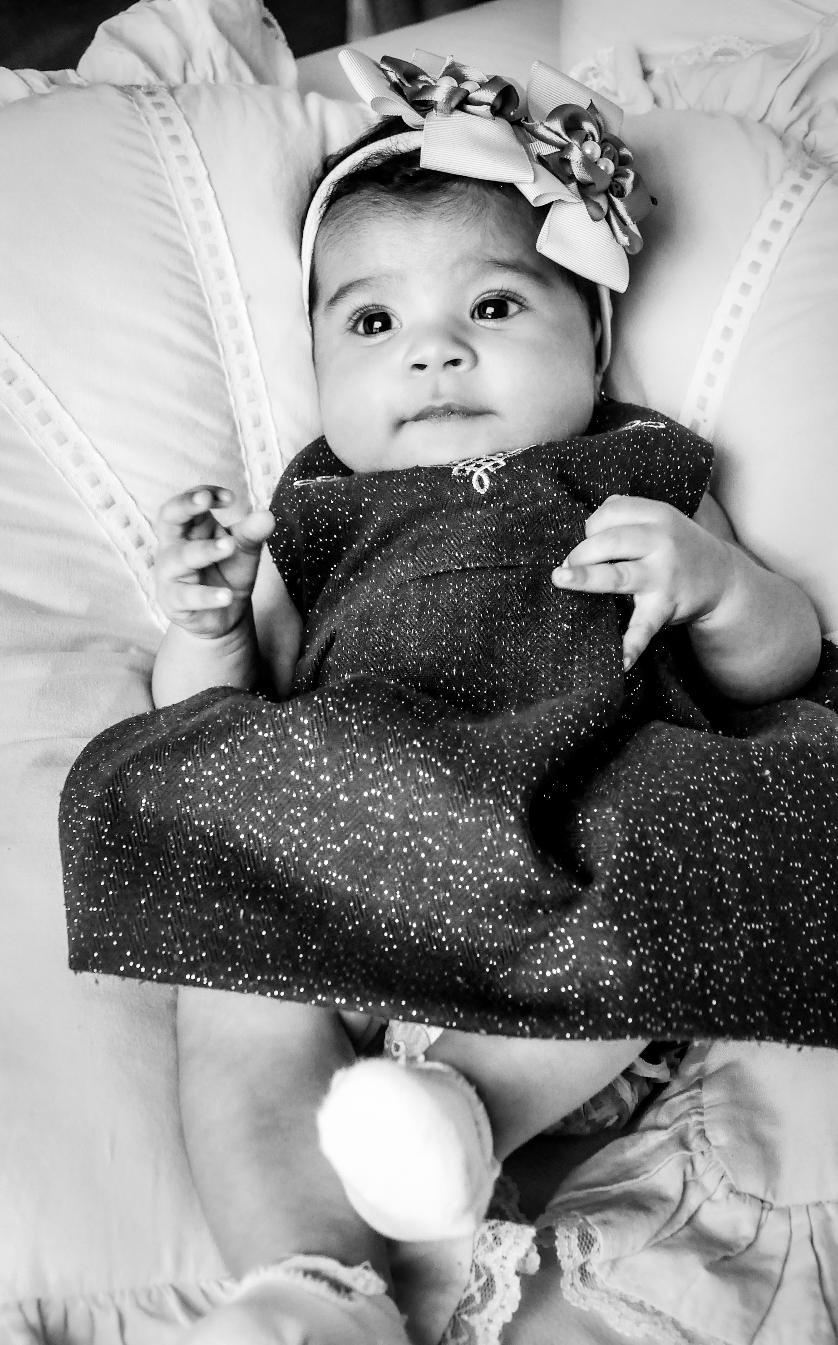 Fofa bebê menina deitada na cama, vestindo um vestido estiloso e faixa na cabeça em uma foto clássica em preto e branco.
