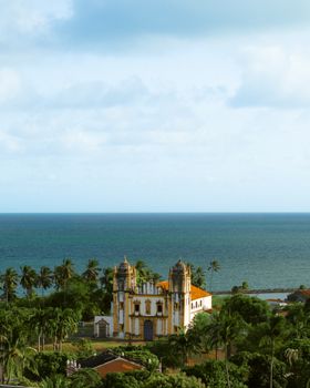 Scenic view of Igreja do Carmo and Atlantic Ocean in Olinda, Brazil, with lush greenery and palm trees.
