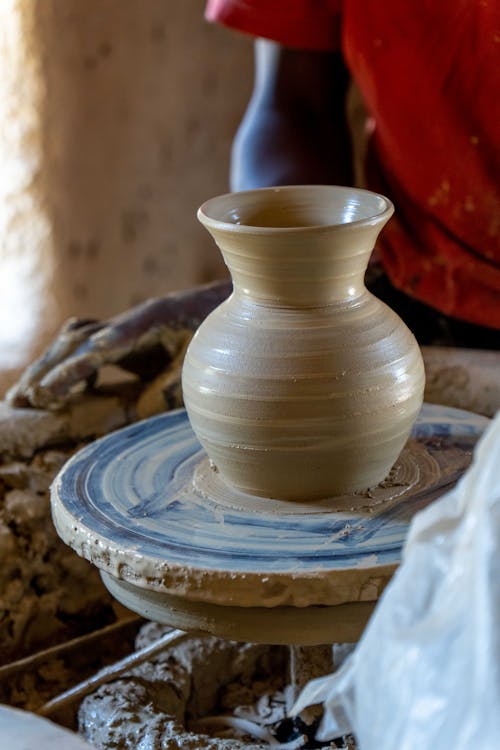 A potter is making a clay vase on a table