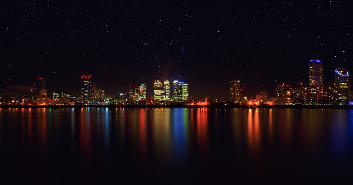City skyline at night with shimmering water reflections and starry sky.