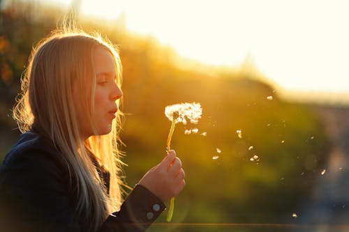A woman blowing a dandelion in the sun