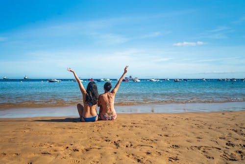 Two women sitting on the beach with their arms up
