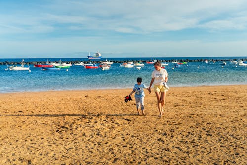 A woman and child walking on the beach near boats