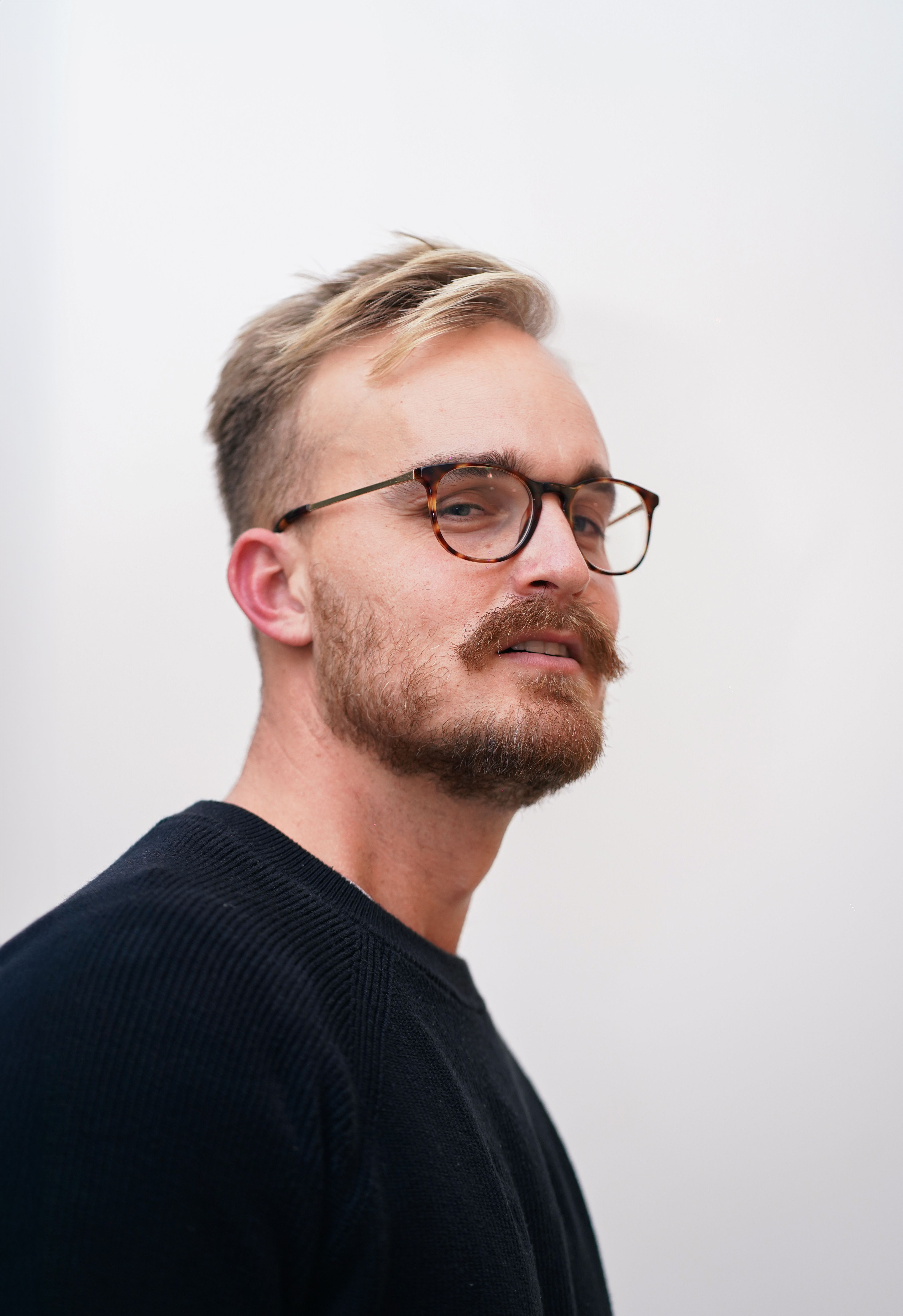Portrait of a stylish man with a beard and eyeglasses, exuding a confident demeanor.