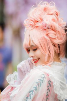 一位留着俏皮粉色头发、穿着精致角色扮演服装的美丽女人，正微笑着