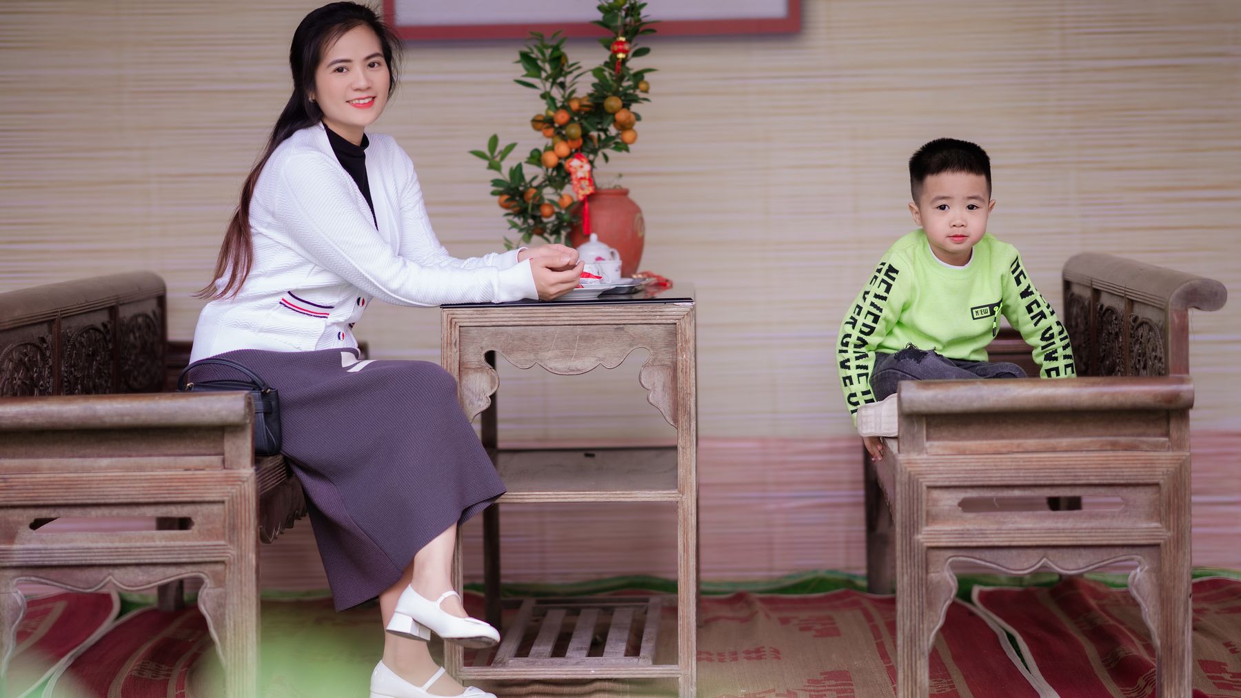 Mother and child seated on wooden furniture with traditional decor, indoors.