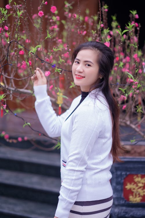 A woman in a white sweater is posing in front of a flowering tree