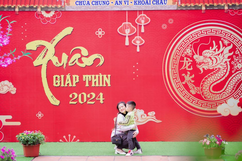 A mother and son pose joyfully in front of vibrant Lunar New Year decorations.