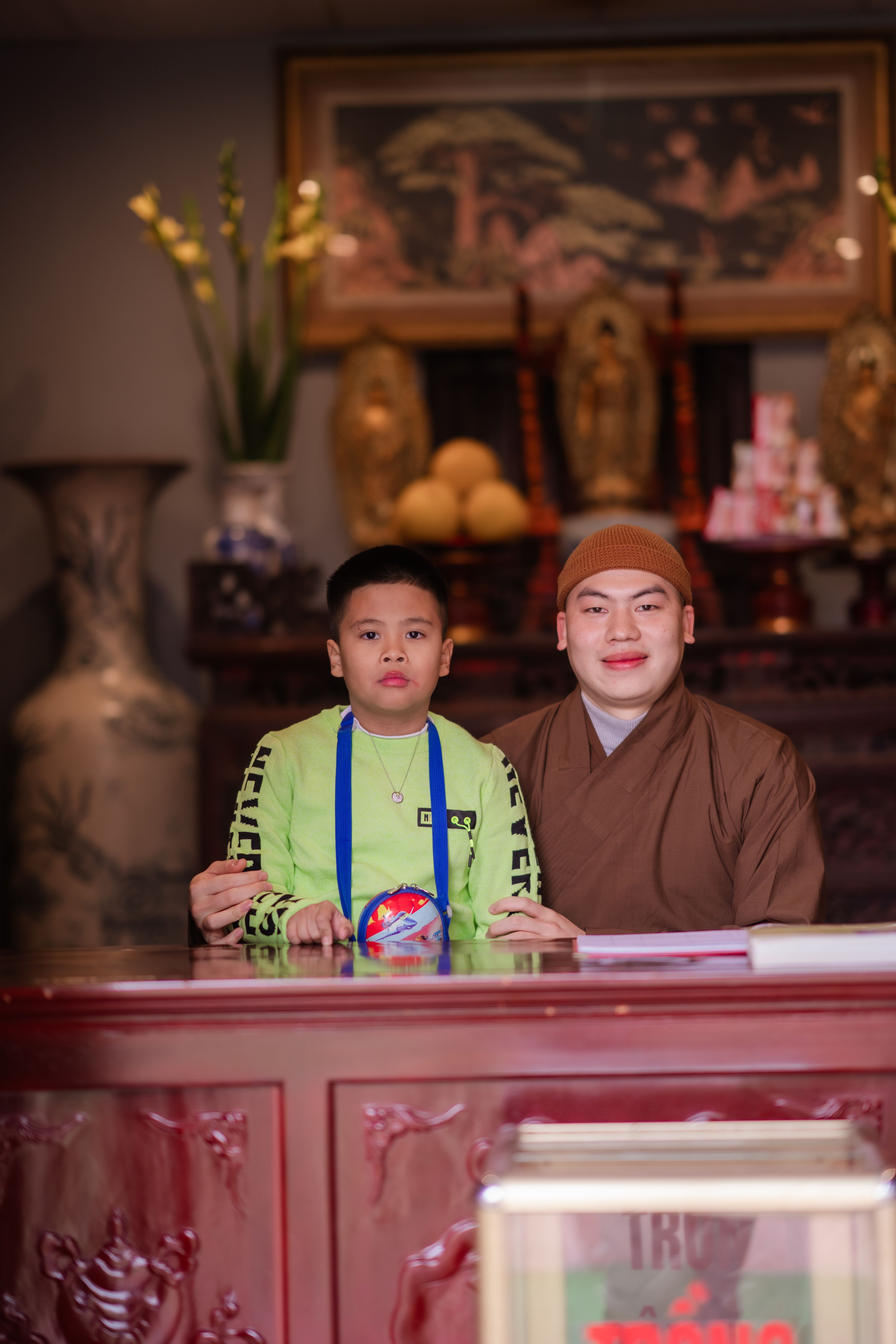 A monk and a boy smile in a traditional indoor setting, reflecting culture and spirituality.