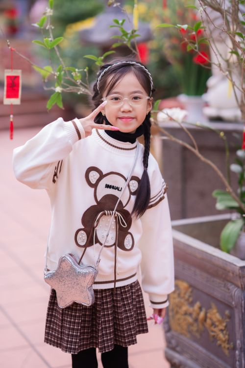 Free Smiling girl in fashionable sweater and skirt making a peace sign indoors. Stock Photo